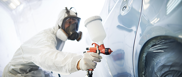 Man in PPE gear spray painting a ca in a spay booth