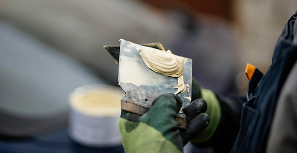 Putty knife with Auto Body Filler on it and a dented car in the background of the image