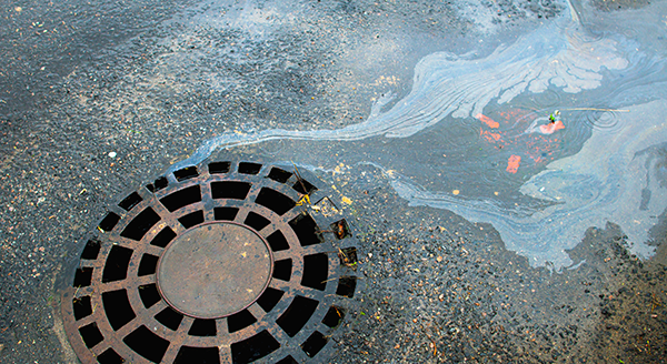 Image of a storm drain with water that has oil like substance flowing into it