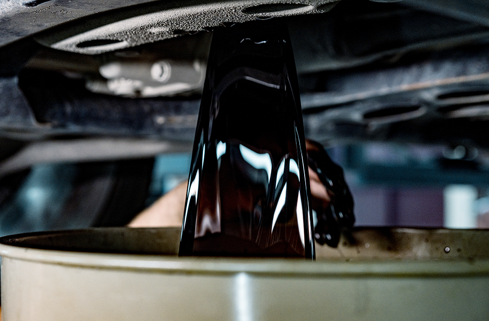 underside of a car draining used engine oil into an oilp an